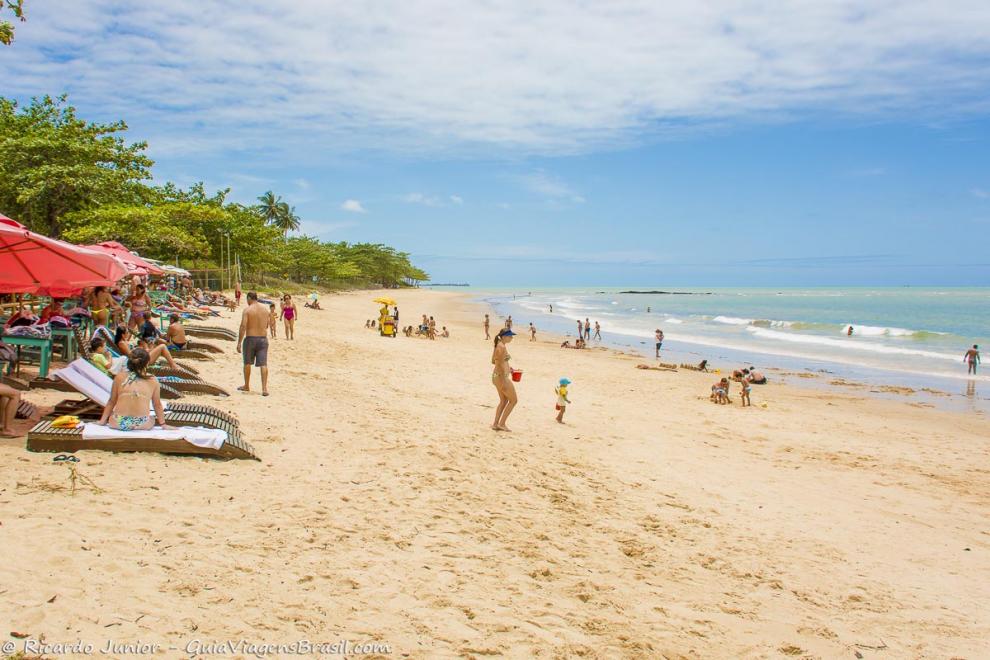 Imagem de turistas nas cadeiras e crianças brincando na beira da Praia de Curuípe.